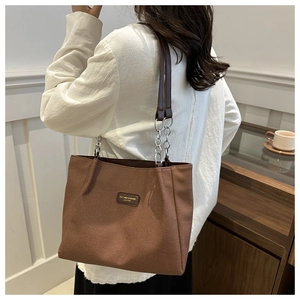 Detail of caramel brown canvas tote bag with metal chain strap and leather patch