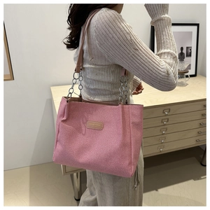 Pink woven tote bag with chain strap shown on shoulder in a cozy indoor setting