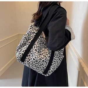 Detail of high-capacity leopard print canvas tote bag with black wide straps on a model