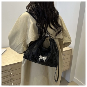 Close-up of black pleated tote bag with silver butterfly charm and metal chain strap