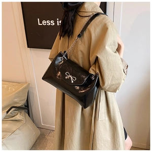 Détail du sac cabas en cuir verni noir avec nœud métallique argenté et bandoulière chaîne
