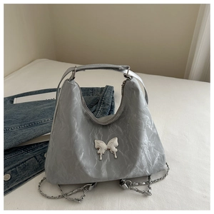 Detailed shot of the metallic butterfly buckle on a silver pleated leather tote bag