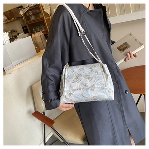 Détail du sac à bandoulière en tissu blanc avec broderie papillon bleue et chaîne
