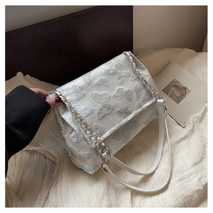 Détails des papillons brodés sur un sac en cuir blanc avec bandoulière chaîne argentée