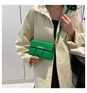 Detail of vibrant green crossbody bag with textured geometric embossing on trench coat