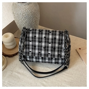 Détail du sac à carreaux noir et blanc avec nœuds brodés et bandoulière chaîne