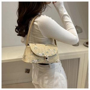 Detail of floral embroidery and gold twist lock on the woven straw underarm bag