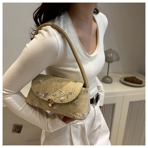 Detailed embroidery of pink flowers and green leaves on a beige woven straw shoulder bag