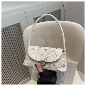 Close-up of cream woven bag with green floral embroidery and gold metal clasp lock