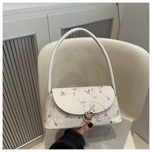 Detail of woven straw shoulder bag with green floral embroidery and gold metal lock