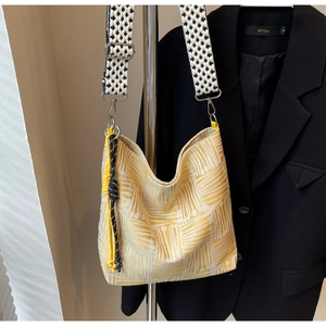 Detailed view of yellow geometric textured tote bag with wide checkered strap on a suit