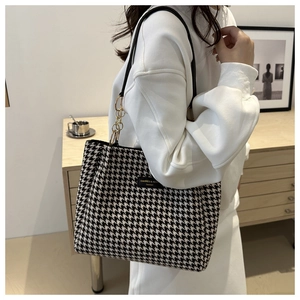 Close-up of black and white houndstooth tote bag with gold chain strap detail