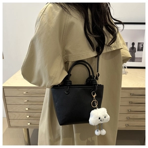 Dettaglio borsa a secchiello nera con ciondolo a nuvola su un trench beige elegante