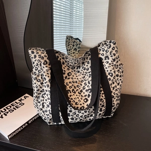 Large leopard print tote bag with black canvas straps and side pocket on wooden surface