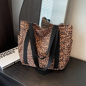 Leopard print canvas tote bag with black handles and side pocket on wooden surface