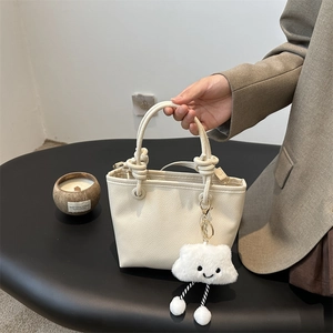Elegante borsa a secchiello beige grana litchi con manico a nodo e ciondolo