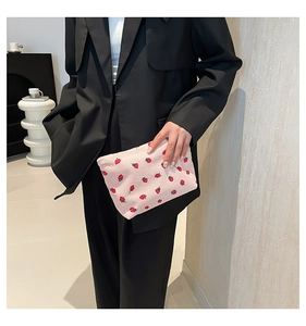 Dettaglio della pochette in velluto a coste rosa con ricamo fragola tenuta da una modella