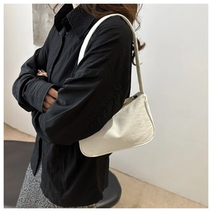 Detailed side view of a white minimalist hobo shoulder bag worn by a model