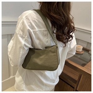 Olive green nylon underarm bag shown on model in a minimalist interior setting