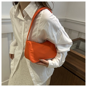 Detailed view of the orange shoulder bag with curved design and canvas texture on a model
