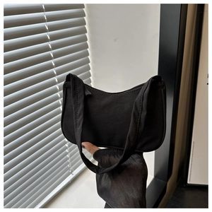 Minimalist black canvas shoulder bag featuring a curved zipper and sleek aesthetic