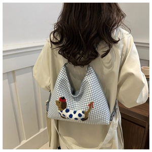 Detail of blue plaid fabric and cute dachshund embroidery on crossbody bag worn by model