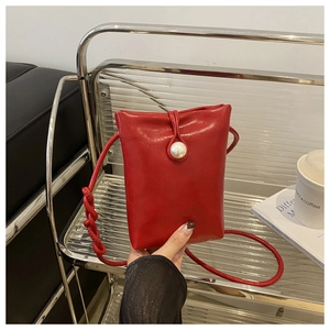 Detailed view of a red mini crossbody phone bag featuring a large decorative faux pearl