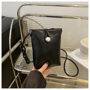 Detail view of mini black crossbody bag featuring a large pearl clasp on silver shelf