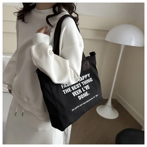 Detail of black nylon tote bag with white text print and brown leather handles