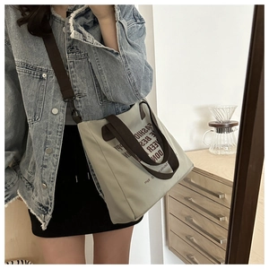 Detail of grey canvas tote bag with fashion lettering and brown adjustable strap