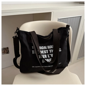 Detail of a large black canvas tote bag with white lettering on a minimalist white chair