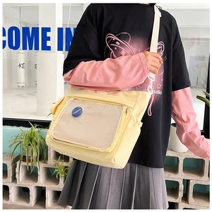 Detail of light yellow canvas tote featuring a transparent mesh pocket and blue badge decoration