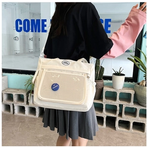 Detail of white canvas tote bag featuring front mesh zipper pocket and fashion patch
