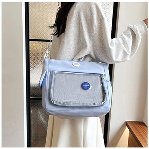 Detail of light blue tote bag with transparent mesh front pocket and fashion badges