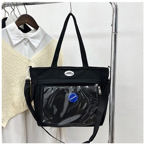 Detail view of the clear PVC front pocket and logo patch on black tote bag