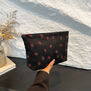 Borsa in velluto a coste nera con stampa a fragole tenuta su sfondo minimalista