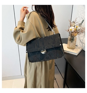 Detail of black pleated faux leather shoulder bag with silver clasp and chain strap