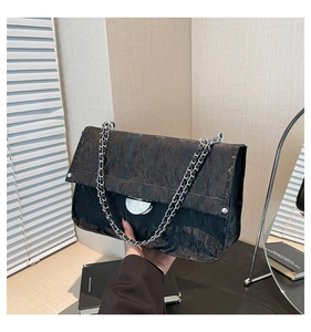 Close-up of black textured leather bag with large silver round clasp and chain strap