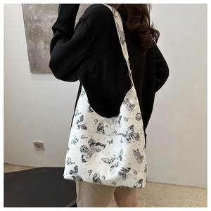 Detail view of large white tote bag featuring black butterfly prints and wide shoulder strap