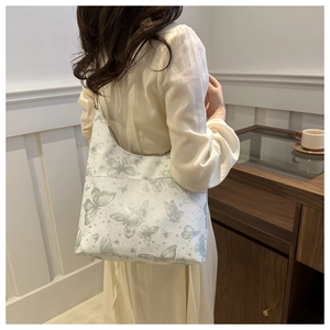 Shoulder shot of a white tote bag with green butterfly prints and sleek PU leather finish
