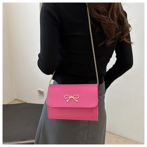 Detail of rose red crossbody bag featuring gold bow buckle and fine metal chain strap