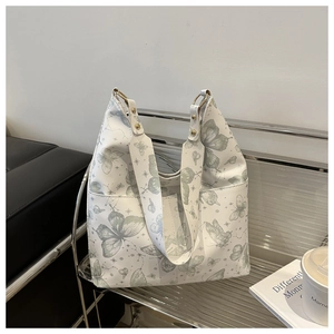 Detail of white bucket bag with green butterfly print and gold hardware on a chair