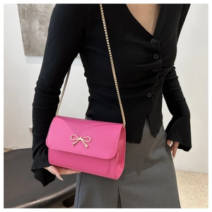 Detail of bright pink crossbody bag with gold bow buckle and chain strap on a model