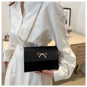 Détail du sac bandoulière en cuir noir avec nœud doré et fine bandoulière chaîne