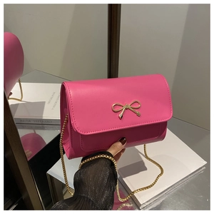 Detail of rose red leather crossbody bag with golden bow clasp and metal chain strap