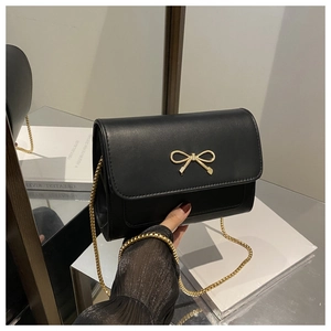 Detail of black mini bag with gold bow clasp and sleek metal chain strap on mirror surface