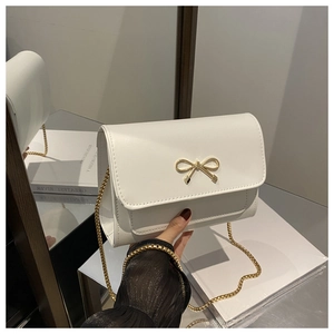 Close-up of white crossbody bag featuring golden bow metal clasp and fine chain strap