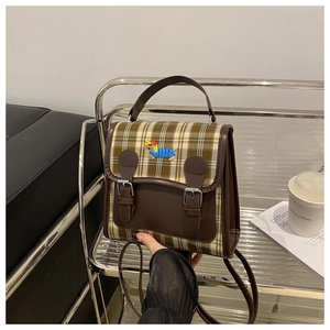 Détail de toile à carreaux et rabat en cuir marron avec broderie de teckel sur le sac à dos