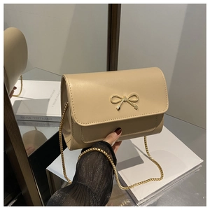 Close-up of beige underarm bag with golden metal bow detail and thin chain strap