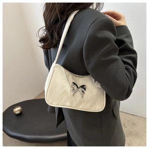 Detail of a creamy white pleated shoulder bag with a metallic butterfly ornament